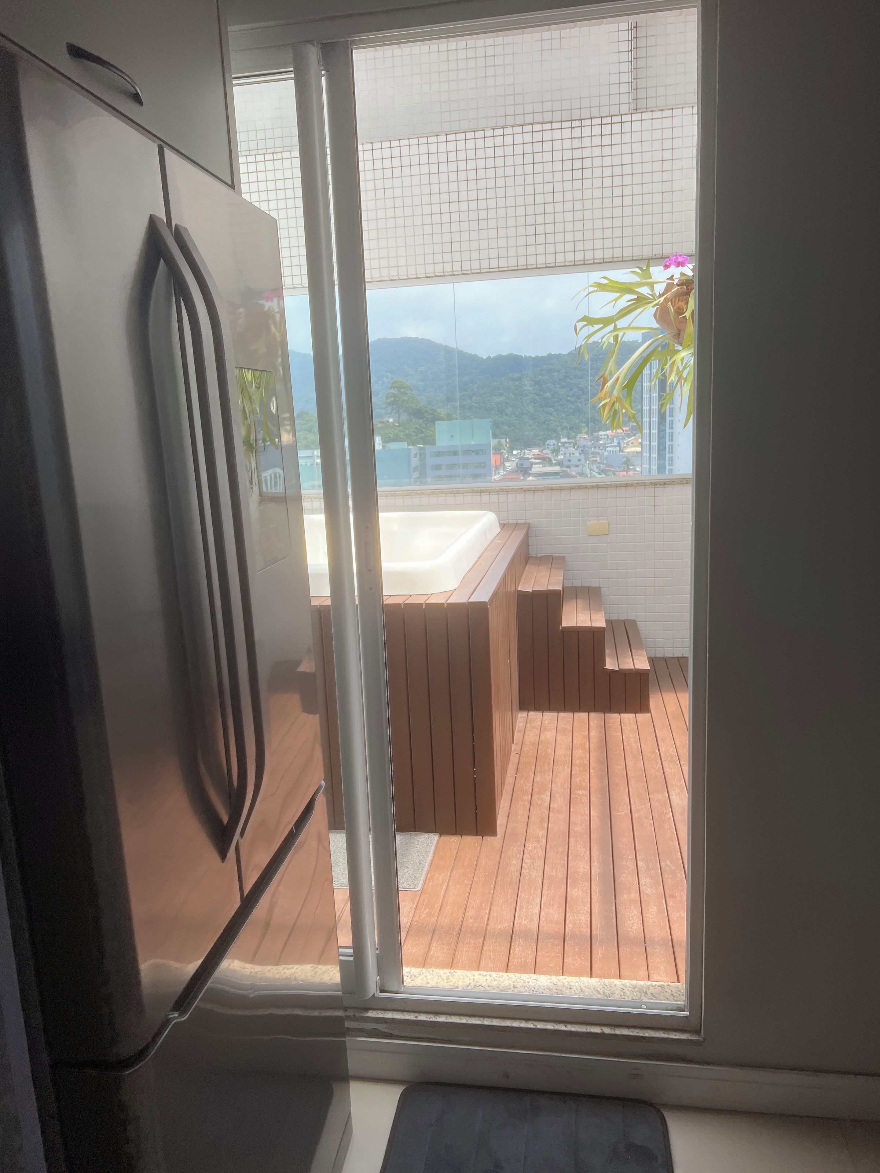 A modern kitchen with a refrigerator, a sliding glass door leading to a balcony with wooden flooring and a hot tub.