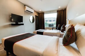 Una habitación de hotel con dos camas, un televisor, una ventana con cortinas y un equipo de aire acondicionado.