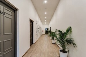 Un pasillo con piso de madera, paredes blancas y una puerta a la izquierda.