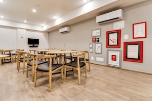 A modern interior with wooden tables and chairs, a flat-screen TV, and various framed artworks on the walls. - Townhouse Gandhi Hall (Indore)