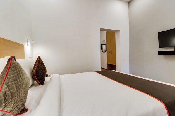 A hotel room with a large bed, a flat-screen TV mounted on the wall, and a wooden door leading to a bathroom. - Townhouse Gandhi Hall (Indore)