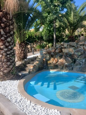 A pool with a stone wall and palm trees.