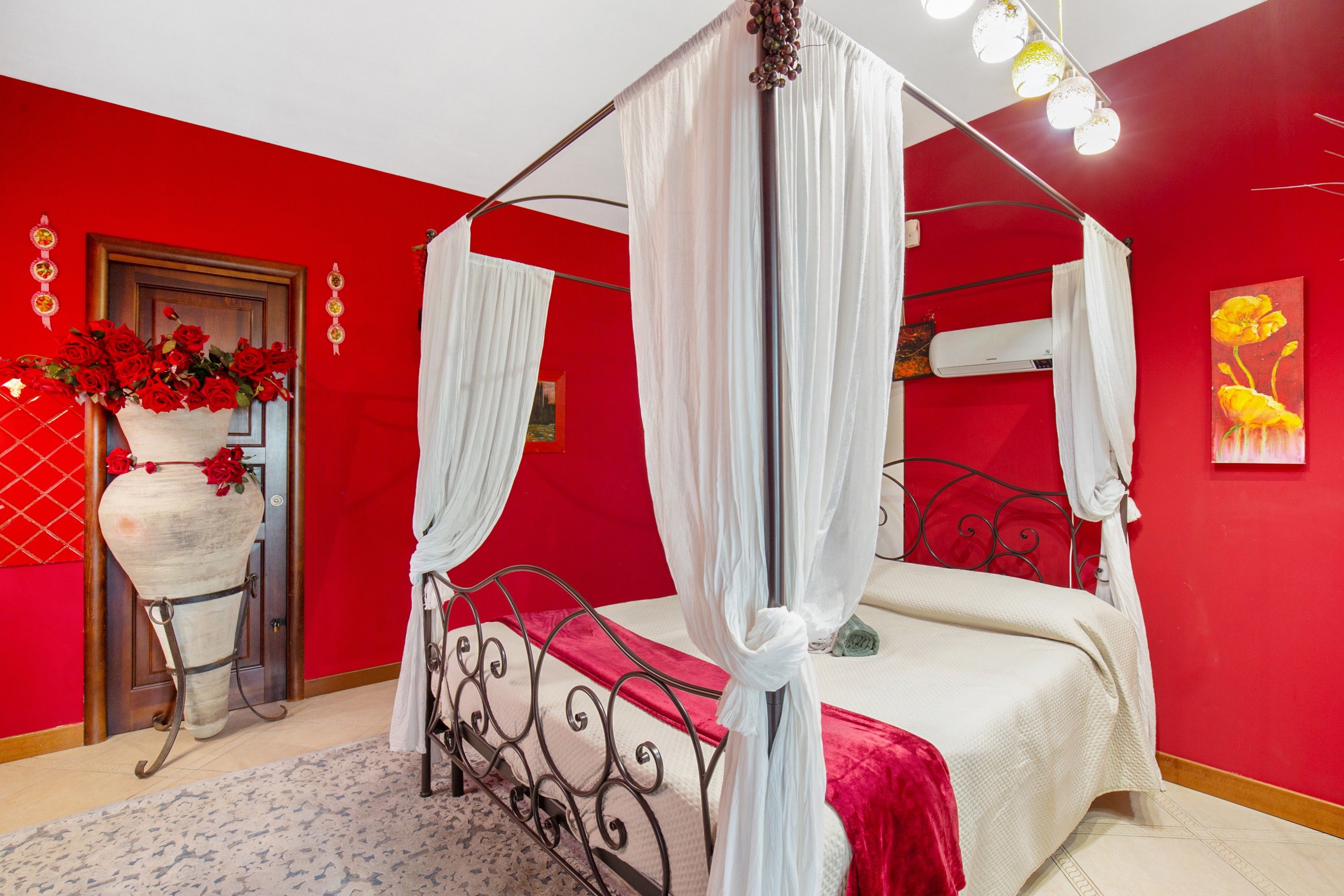 Ein Himmelsbett mit Baldachin, eine rote Wand und ein Blumenbild.