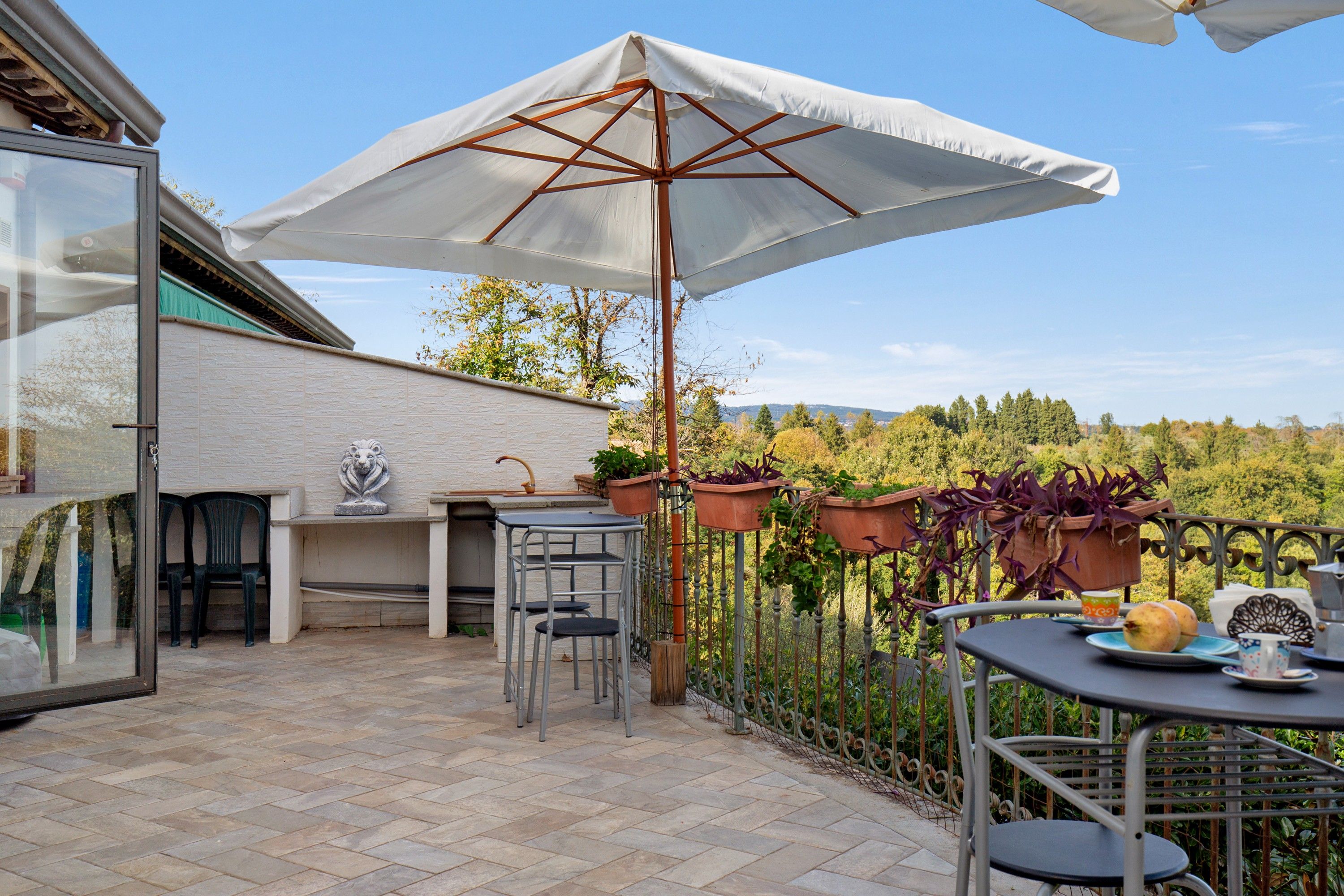 Eine Terrasse im Freien mit Tisch, Stühlen, Sonnenschirm und Blumentöpfen.