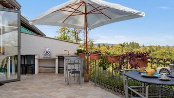 Eine Terrasse im Freien mit Tisch, Stühlen, Sonnenschirm und Blumentöpfen.