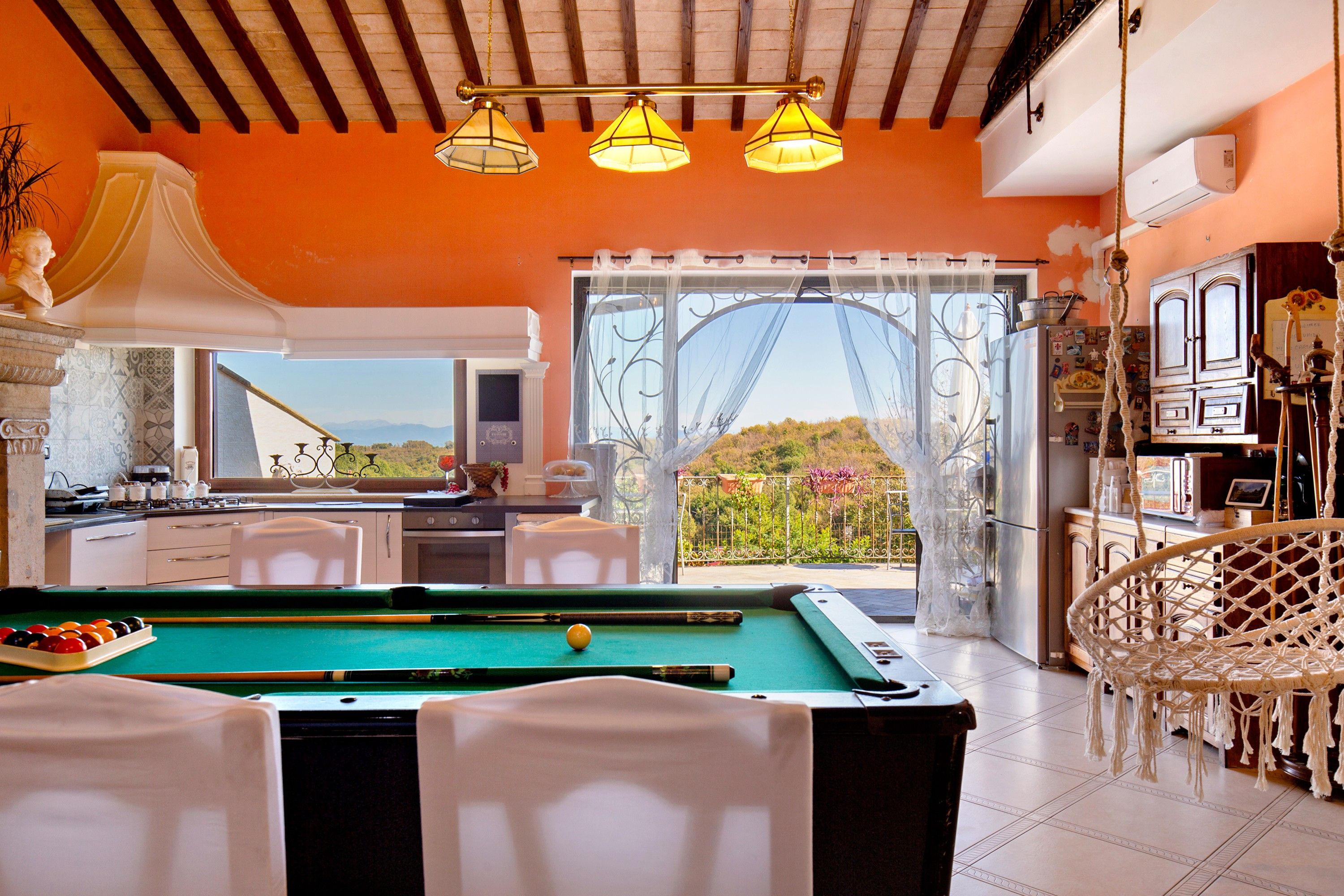 A pool table in a room with a view of the outdoors, a kitchen area, and a dining space with a view.