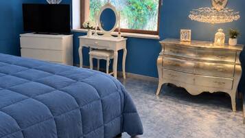 Un dormitorio con una cama azul, un aparador blanco, una tocador con espejo y un televisor sobre un mueble.