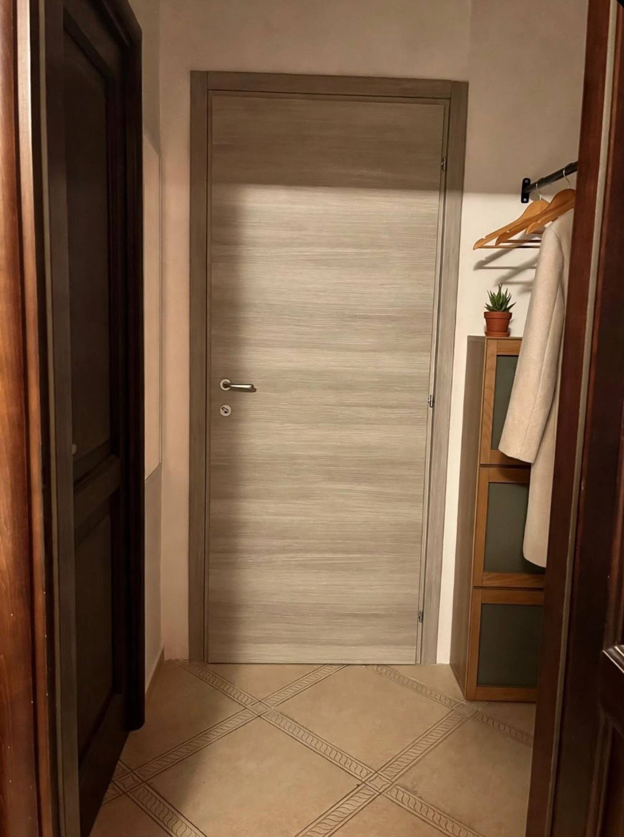 Una puerta cerrada con un ojo de cerradura y un pomo, un estante de madera con una planta en maceta, y una toalla colgada.