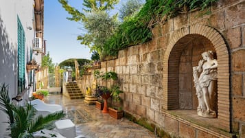 A courtyard with a statue, stone walls, and potted plants.