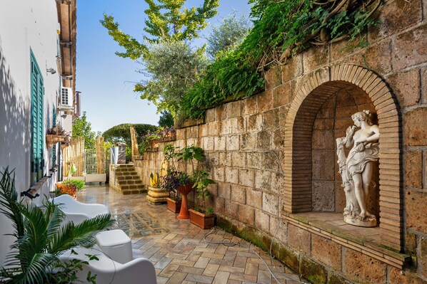 Une cour avec une statue, des murs en pierre et des plantes en pot.
