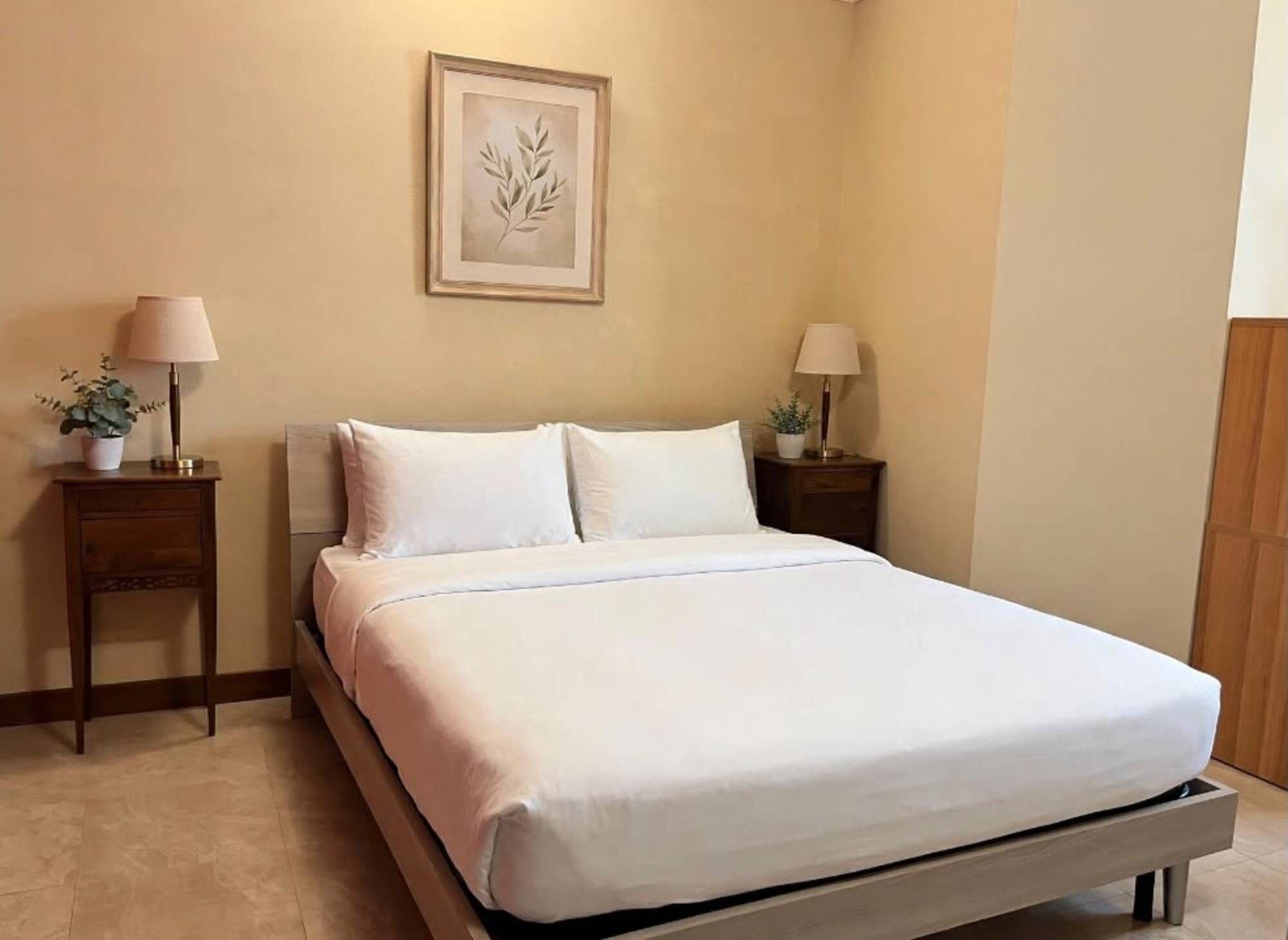 Una cama bien hecha con ropa blanca, dos mesitas de noche con lámparas y una obra de arte enmarcada en la pared.