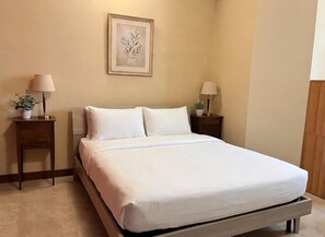 Una cama bien hecha con ropa blanca, dos mesitas de noche con lámparas y una obra de arte enmarcada en la pared.