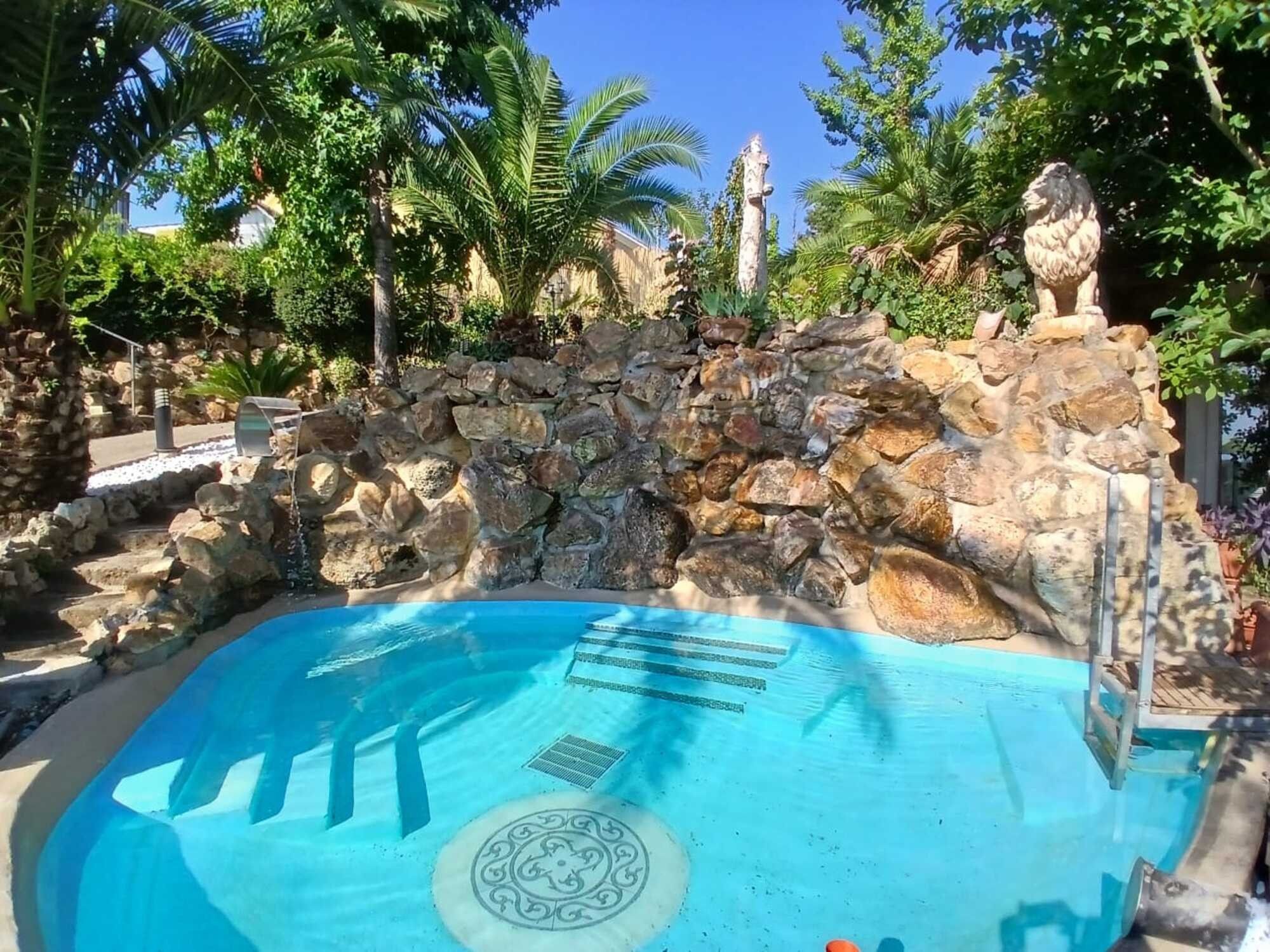 Una piscina con una pared de piedra y palmeras al fondo.