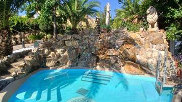 Una piscina con una pared de piedra y palmeras al fondo.