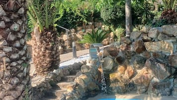 A pool area with a stone wall, palm trees, and a waterfall feature.