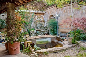 Un jardin avec un mur de pierre, un petit étang et un pont en bois.