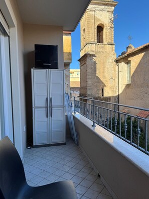Ein Balkon mit Fernseher auf einem Schrank, Geländer und Blick auf ein historisches Gebäude mit einem Glockenturm.
