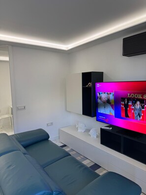 Ein modernes Wohnzimmer mit einem großen Flachbildfernseher an der Wand, einem blauen Sofa und einem weißen Konsolentisch mit Dekoration.