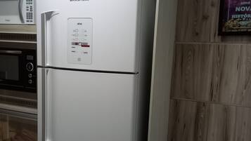 A white refrigerator with a digital control panel, a microwave above it, and a wooden wall panel.