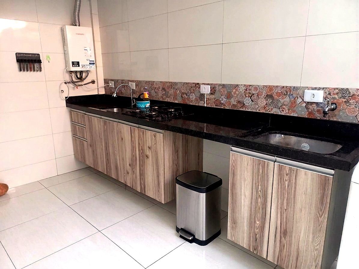 A kitchen with a gas stove, sink, and a trash bin.