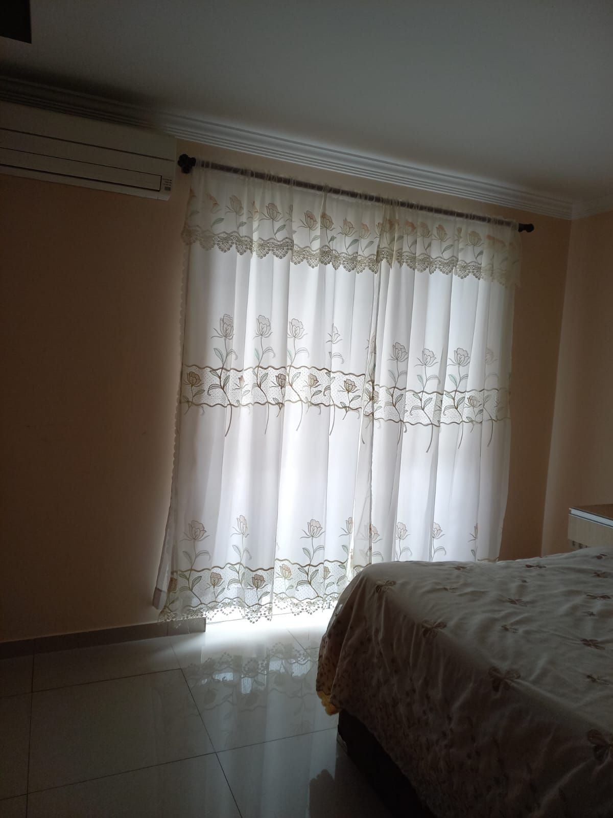 A bedroom with a bed, a window with sheer curtains, and a radiator.