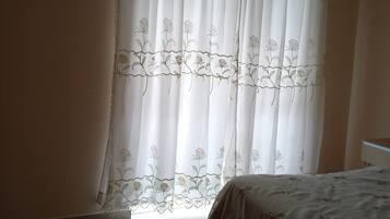 A bedroom with a bed, a window with sheer curtains, and a radiator.