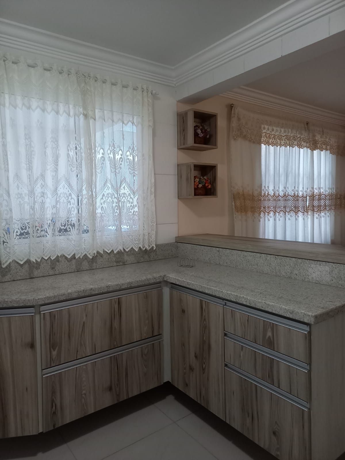 A kitchen with wooden cabinets, a granite countertop, and a window with lace curtains.
