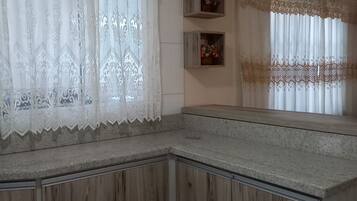 A kitchen with wooden cabinets, a granite countertop, and a window with lace curtains.