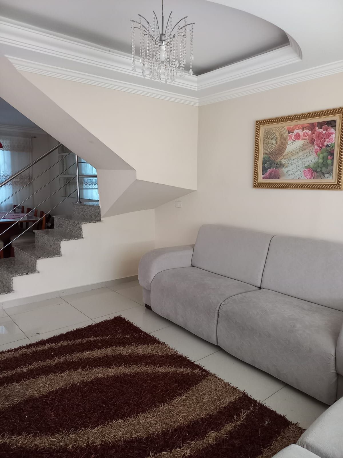 A living room with a grey sofa, a brown shag rug, a chandelier, and a staircase leading to another level.