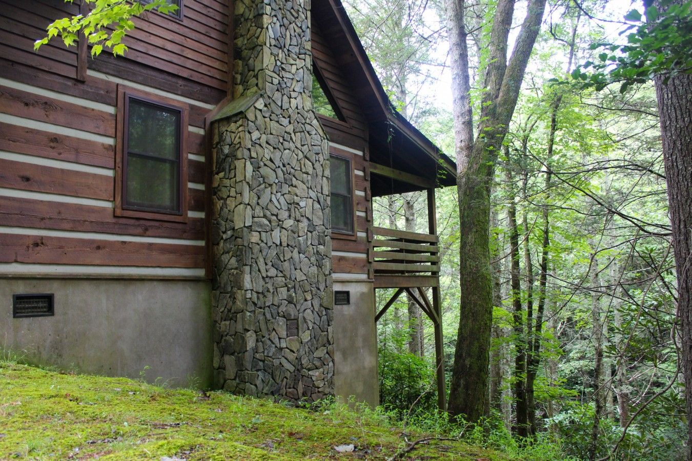 Una baita con camino in pietra, esterno in legno e veranda con vista sulla foresta.
