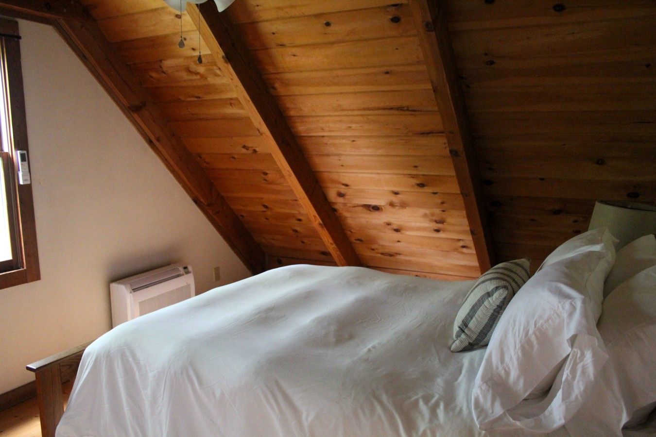 Une chambre avec un plafond en pente, un lit avec une literie blanche et une fenêtre sur le côté gauche.