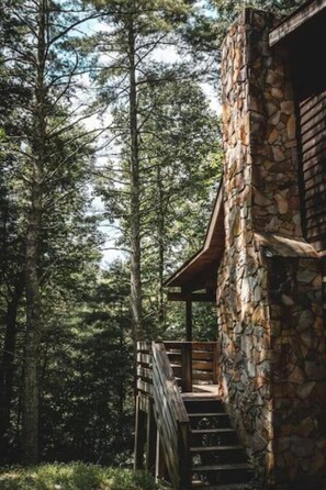 Ein Steinhaus mit einer Holztreppe, die zu einer Terrasse führt, umgeben von hohen Bäumen.