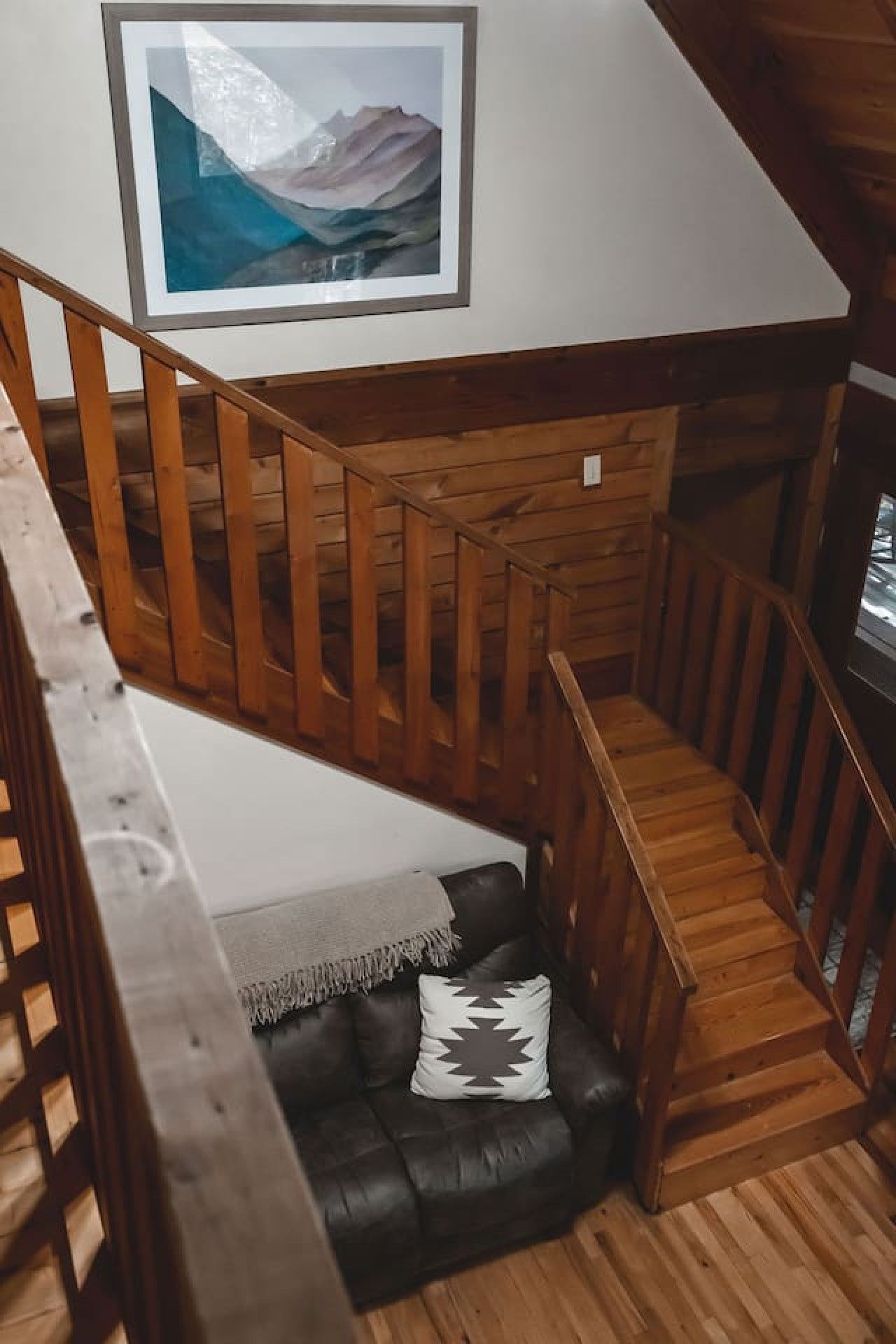Una escalera de madera que baja a un nivel inferior con un sofá de cuero negro y un cojín decorativo.