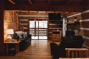 L’intérieur d’un chalet accueillant, avec un plancher en bois, un canapé, un fauteuil, une petite table et un téléviseur fixé au mur.