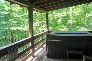 Un bain à remous sur une terrasse en bois, avec vue sur une forêt.