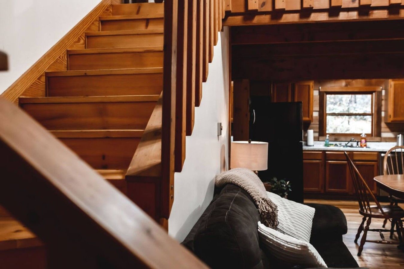 A wooden staircase leading to a kitchen with wooden cabinets and a window.