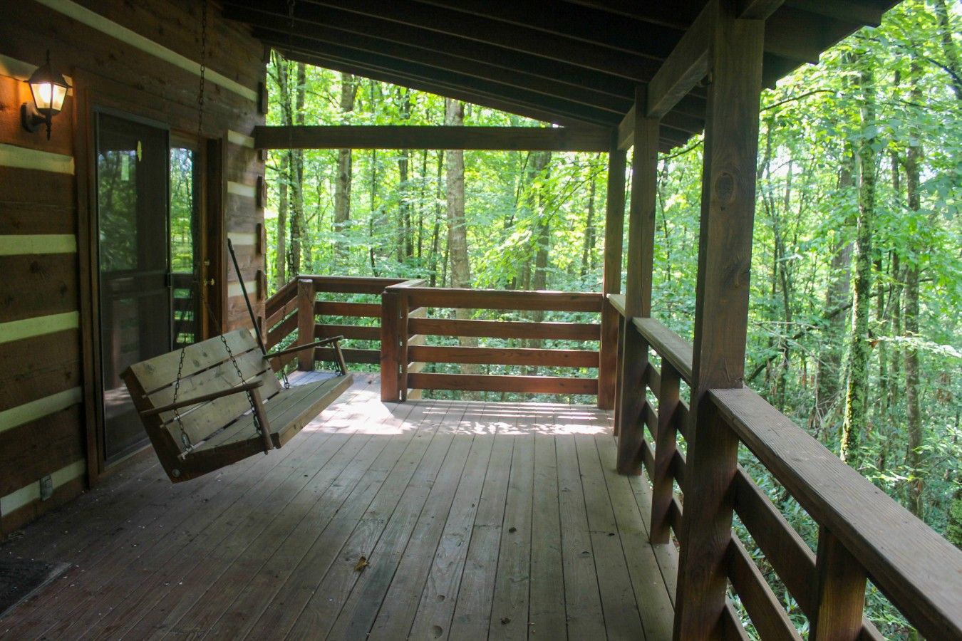 Une terrasse en bois avec un fauteuil suspendu et une porte vitrée donnant sur une zone boisée.