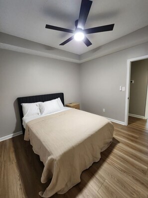 Un dormitorio con una cama, ventilador de techo y suelo de madera.