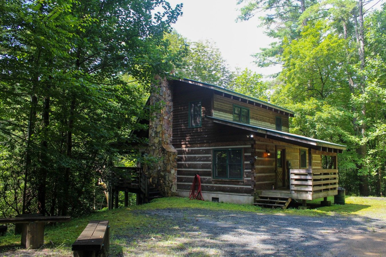 Une cabane rustique avec une cheminée en pierre, une véranda et une allée gravillonnée.