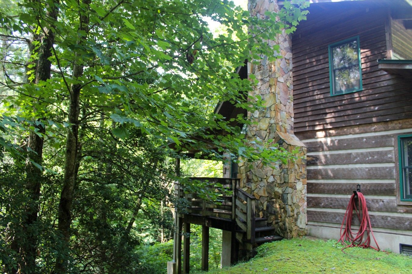 A rustic cabin with a stone wall, wooden deck, and a red hose.