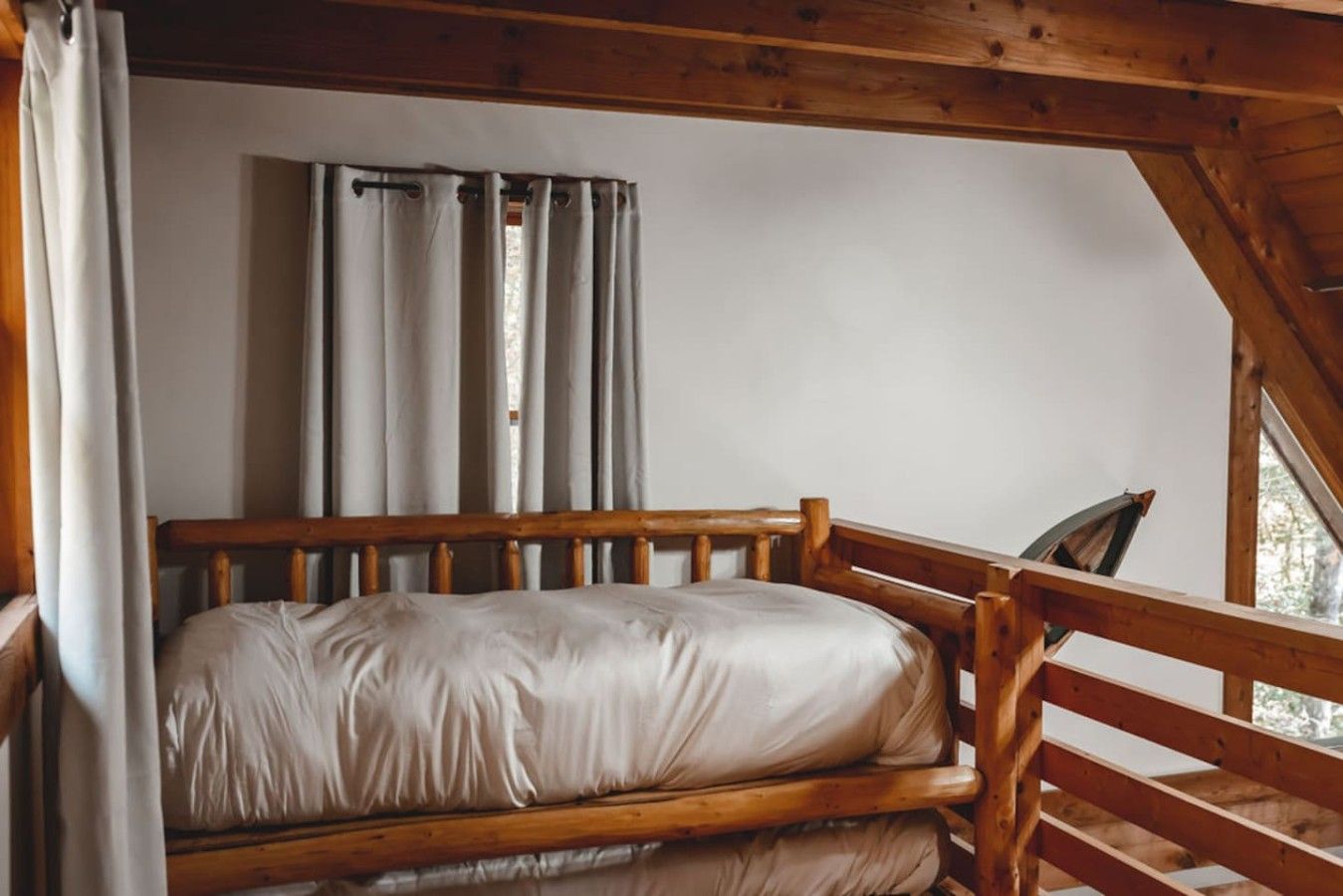 A wooden bunk bed with a mattress and pillows, a wooden headboard, and a window with curtains.