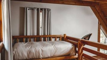 A wooden bunk bed with a mattress and pillows, a wooden headboard, and a window with curtains.