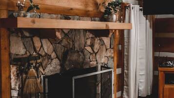 Ein gemütliches Wohnzimmer mit Kamin aus Stein, Holzbalken, einer Ledersofa und einem an der Wand befestigten Fernseher.