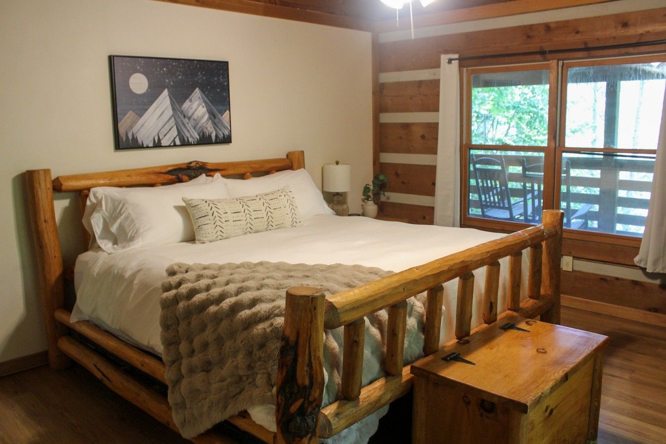 A wooden bed with a headboard, a night sky painting, and a window with a view of trees.