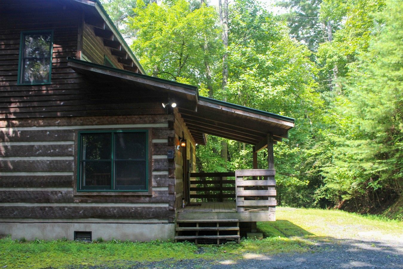 A rustic log cabin with a porch and a window, surrounded by dense forest.