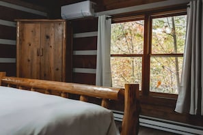 Een houten kamer met een bed, een houten bankje, een kledingkast en een raam met uitzicht op bomen.