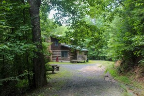 Ein rustikales Blockhaus mit Veranda, umgeben von dichtem Wald.
