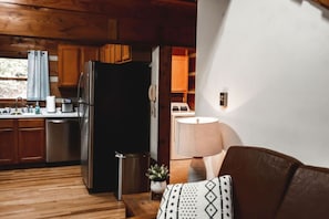 Een houten interieur met een keuken, een eettafel met een lamp en een bank met een gestreept kussen.