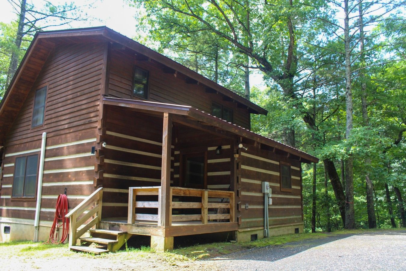 Une cabane en rondins dotée d’une véranda, entourée d’arbres.
