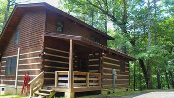 Une cabane en rondins dotée d’une véranda, entourée d’arbres.